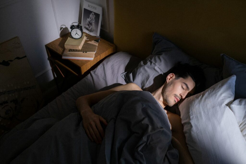 A person peacefully sleeping in bed with a small alarm clock glowing softly on the bedside table